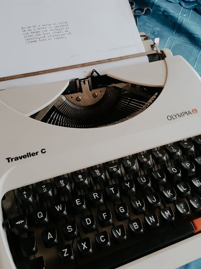 From above of stylish white vintage typewriter on blue cloth in bright room
